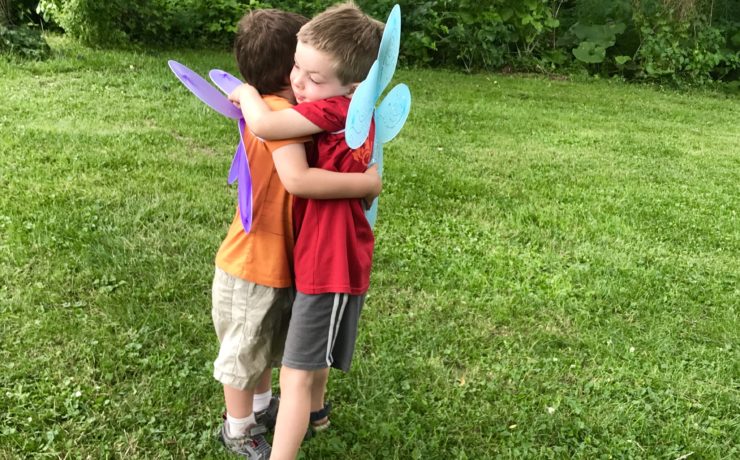 Two children wearing butterfly wings give one another a hug.