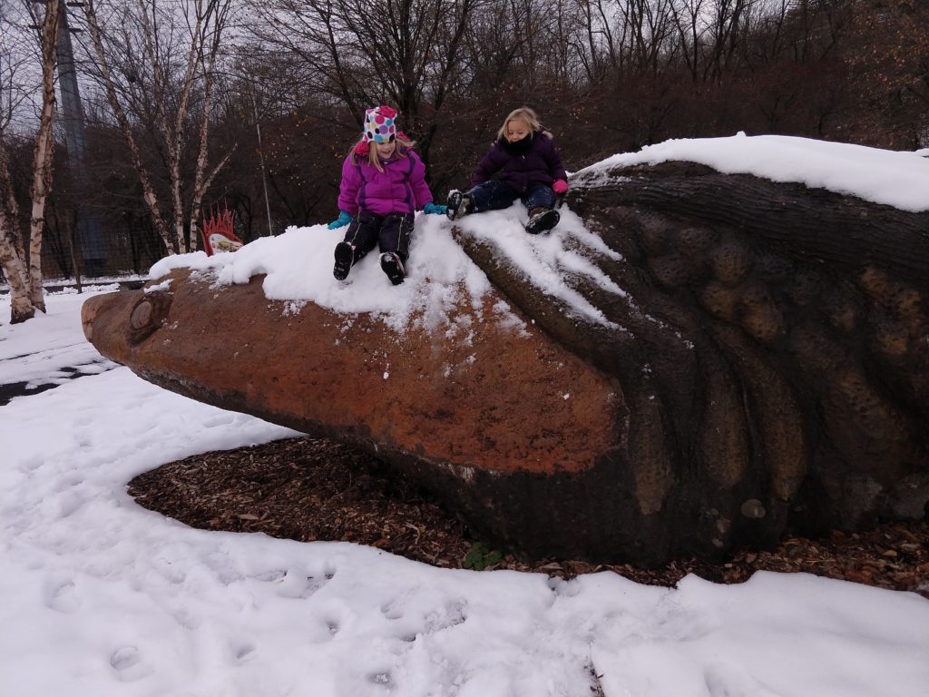 Two small children bundled in cold weather gear sit atop a snow covered Gaia.