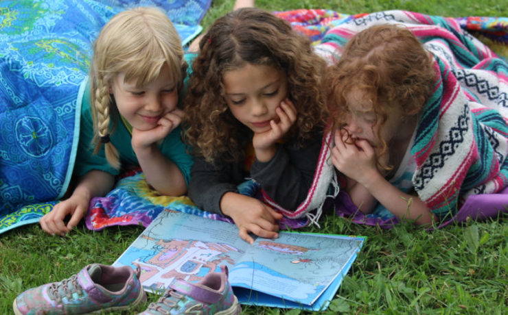 Three children lay on the grass and read a book together.
