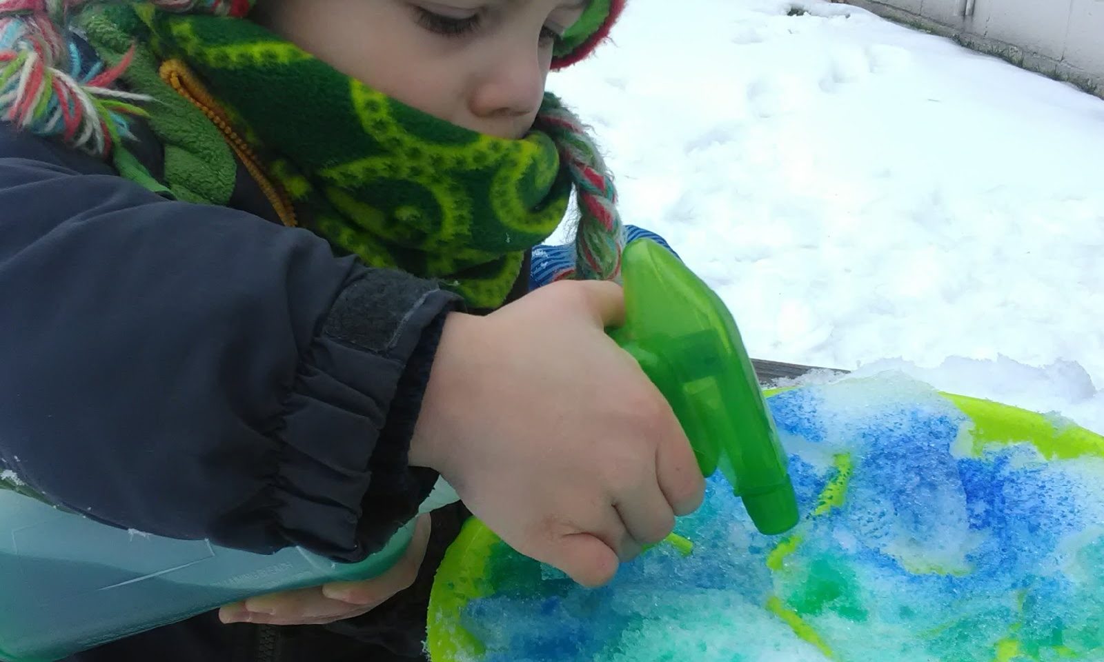 Small child spraying snow with colored water.