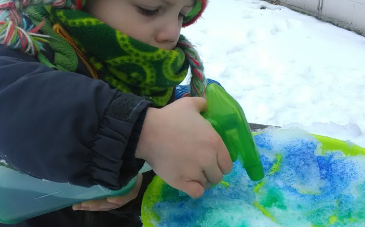 Small child spraying snow with colored water.