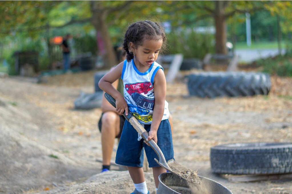 Small child shovels dirt into a bucket.