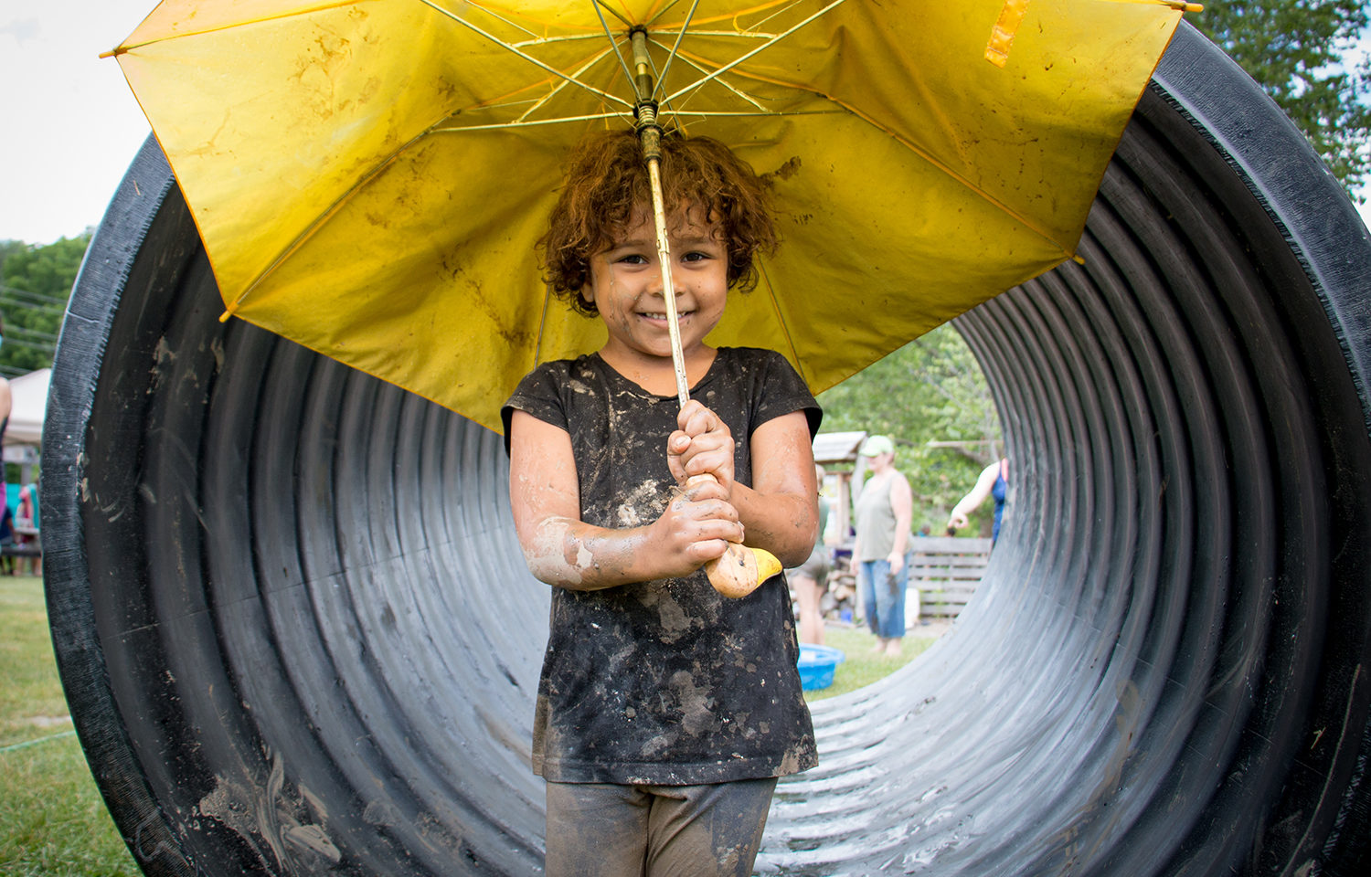 Small child holding a broken umbrella in front of the honaz tube.