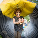Small child holding a broken umbrella in front of the honaz tube.