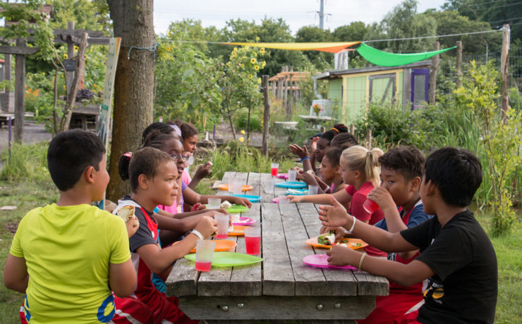 Many young children sit together at a long wooden picnic table.