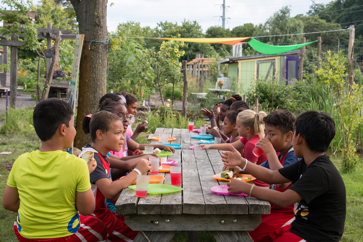 Many young children sit together at a long wooden picnic table.