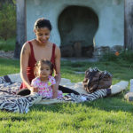 Adult and baby have a picnic in front of ICG troll house.