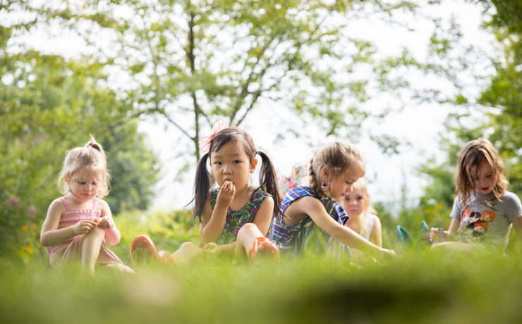Several young children sit next to one another on the grass.