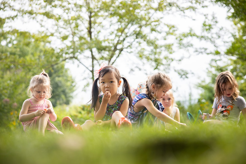 Several young children sit in the grass together. 