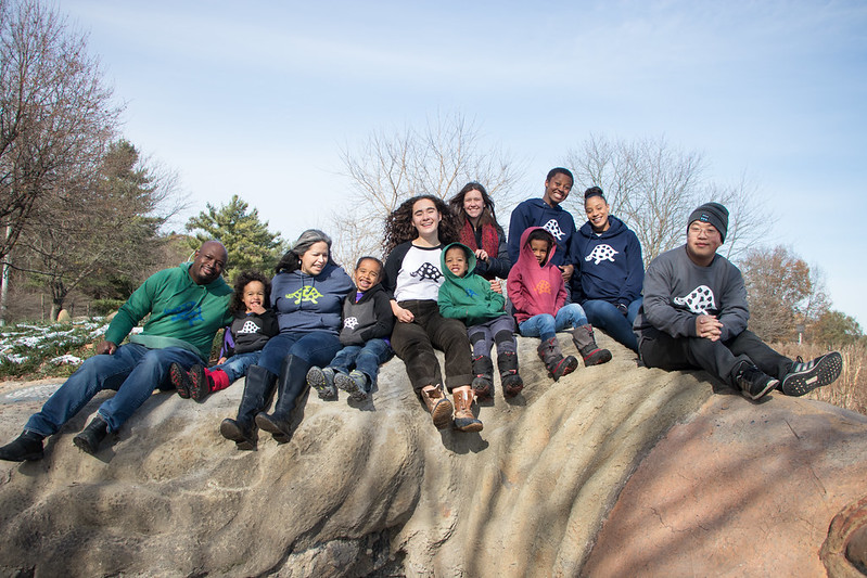 Several people sit atop Gaia the turtle while wearing ICG logo branded gear. 