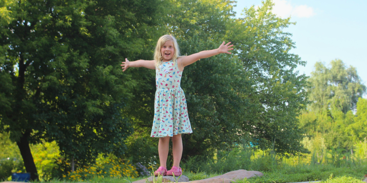 Child throwing her arms out wide, smiling and happy after climbing Gaia on her own.