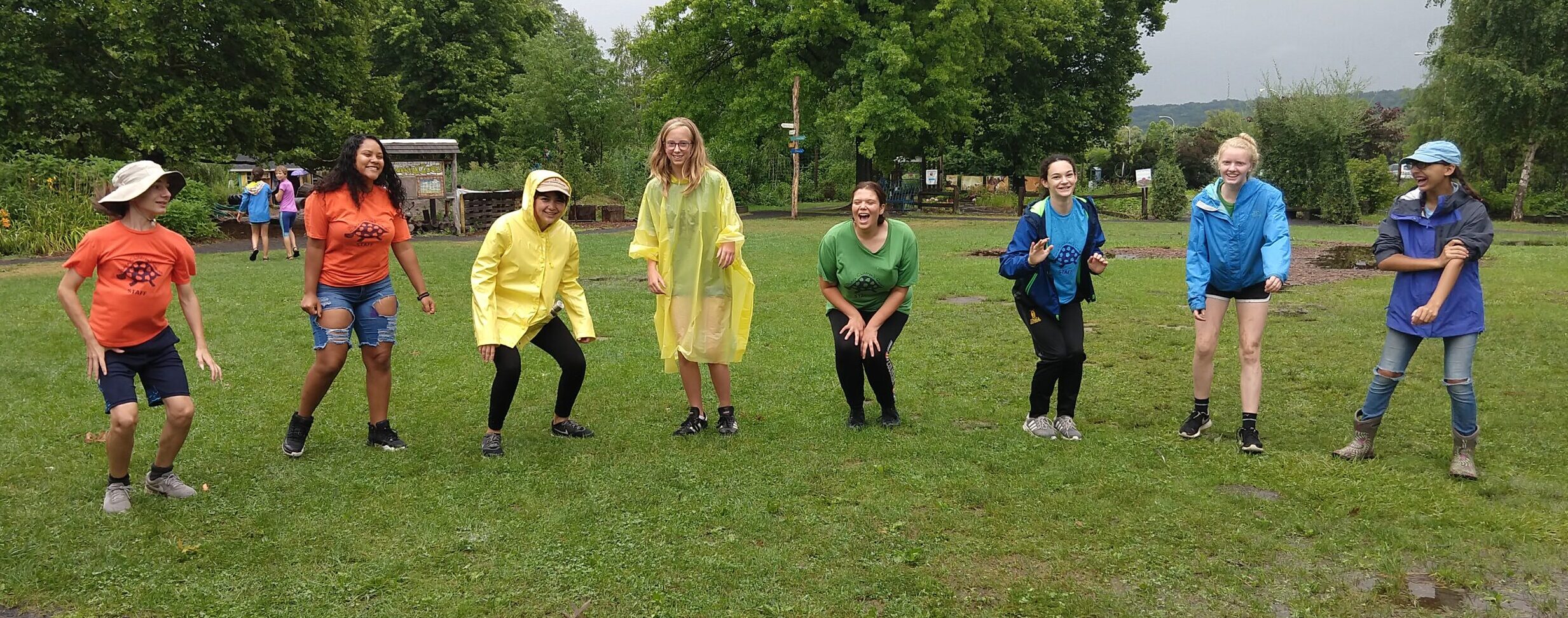 A group of eight people in rainbow colors stand in a line, laughing outdoors