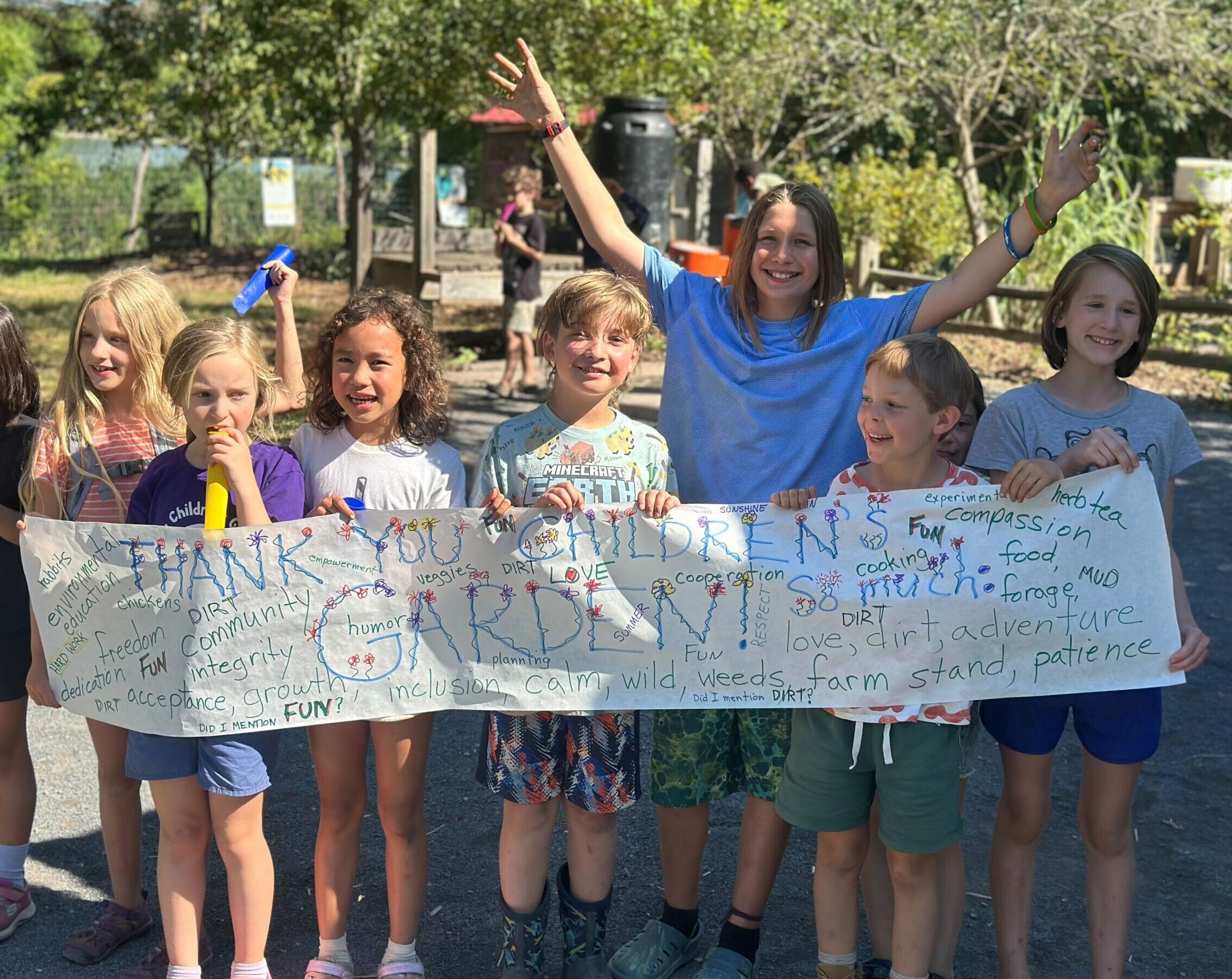 A group of children holds a banner that says thank you ithaca childrens garden