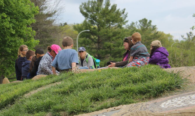A group of adults and kids sits on Gaia, the turtle sculpture's back.