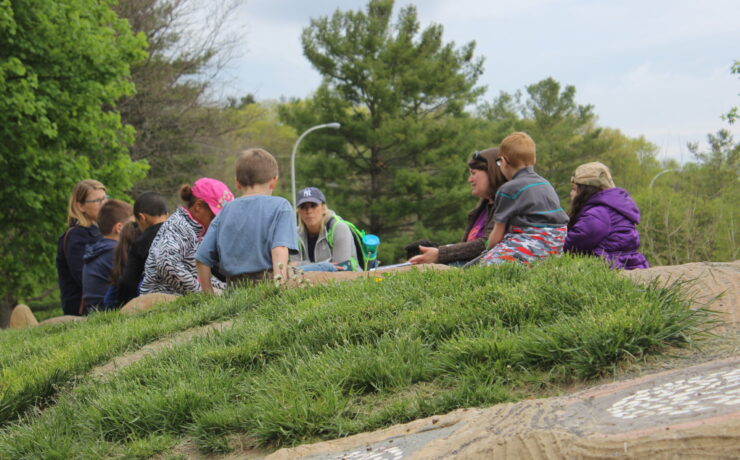 A group of adults and kids sits on Gaia, the turtle sculpture's back.