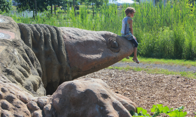 A child sits on Gaia the turtle's snout in a sunny setting.