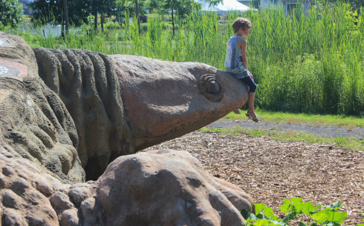 A child sits on Gaia the turtle's snout in a sunny setting.
